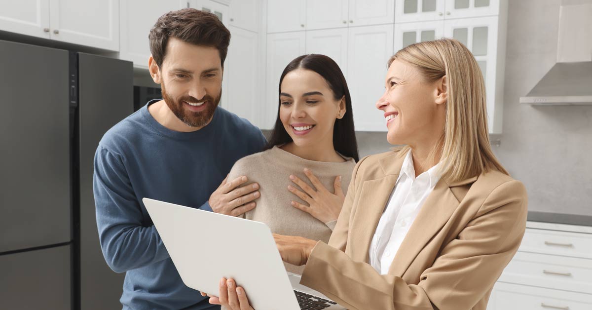 Couple and real estate agent smiling while looking at something.