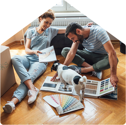 Smiling couple sitting on the floor with a small dog, looking at color samples and flooring options while planning home decor