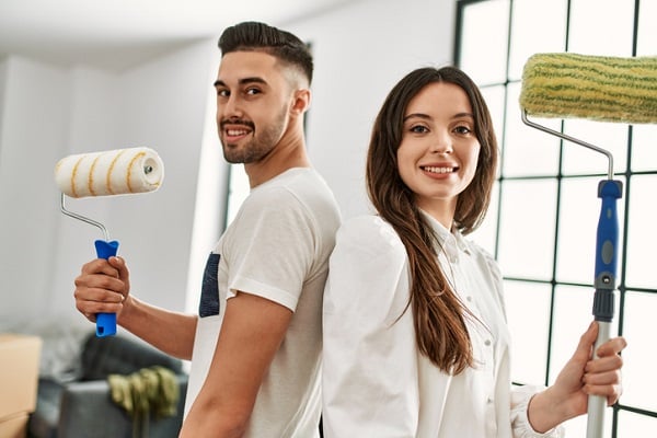2025 Paint Color of the Year |Young couple smiling and looking at each other while holding painting tools, taking a break from painting the walls in their new home