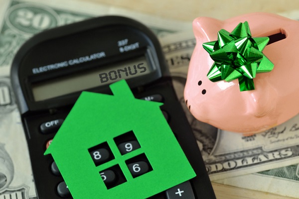 Offering Buyer Incentives: Do's and Don'ts | An old-school calculator with the word BONUS on its display. A green paper cutout of a house rests on the keypad. A piggy bank with a green bow is to the right of it. Everything is on a pile of money.