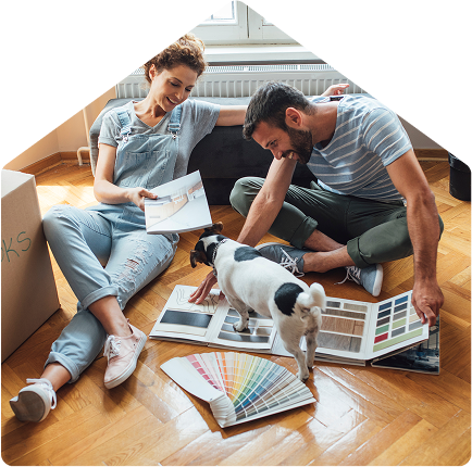 Smiling couple sitting on the floor with a small dog, looking at color samples and flooring options while planning home decor