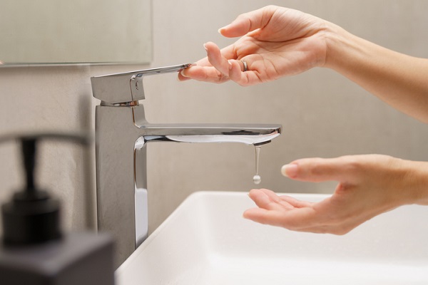 Close up of woman's hand turn on faucet and a drop of water dripping out into hand at white ceramic wash basin in modern design bathroom