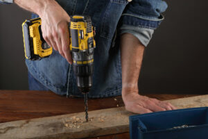a young person drills a hole in the plank on a gray background using power drill