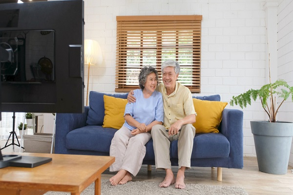 Senior asian couple holding remote control while watching television in home living room with happiness, old people retirement routine lifestyle