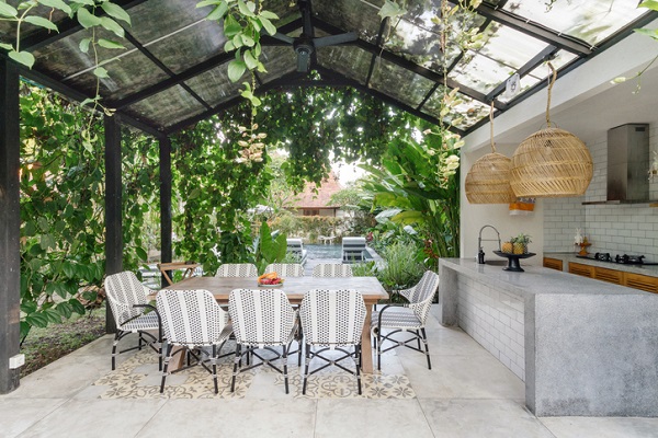 Open kitchen with empty dining room table and chairs outside, against green fresh plants on background