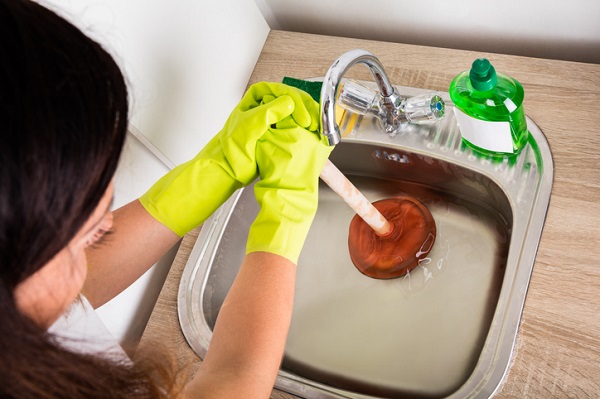 Close-up Of Person Using Plunger In The Kitchen Sink