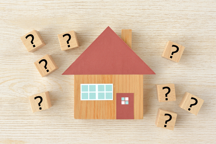 A wooden model house with a red roof surrounded by small wooden tiles with question marks on them to indicate questions about showing homes
