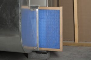 A wood-framed, blue furnace filter sticking halfway out of a furnace.