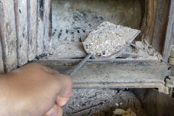 Person cleaning their fireplace of ash to protect chimney