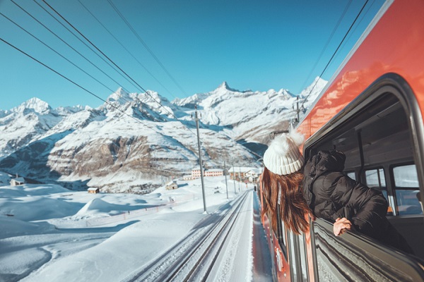Happy woman traveler looks out from window traveling by train in beautiful winter mountains, winter travel