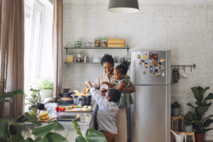 Happy Black mother, daughter, and son preparing spaghetti and vegetables for lunch over a kitchen sink.
