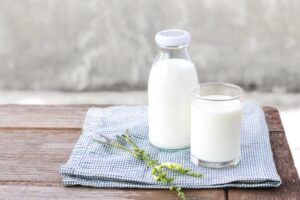 A glass bottle and glass filled with milk resting on a light-blue gingham cloth on a wood table