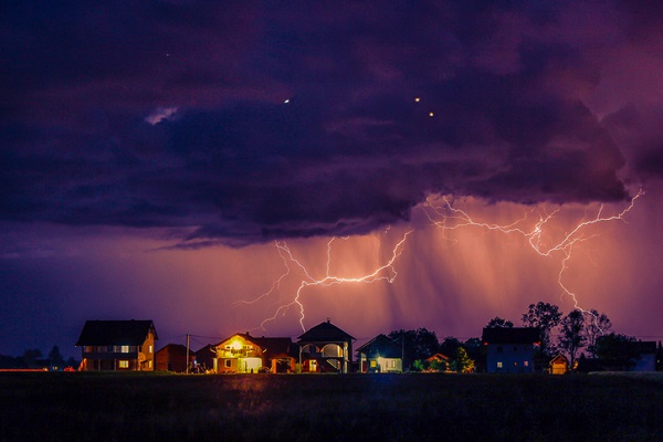 A big thunderstorm over a city. Lighting is visible and the clouds look purple.