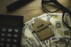 Selective focus of pen, glasses, calculator, money and cardboard home written with Down Payment on wooden background.