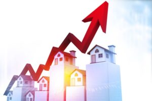 Several wooden-model houses on a bar graph with a red arrow trending upward. Signifying rising cost of home ownership