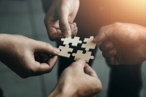 The hands of four different people each holding a different puzzle piece. The picture represents the idea of finding solutions. 