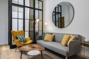 Colorful and cozy living room with a designer armchair and sofa along with a round decorative mirror and glass wall and mirrors