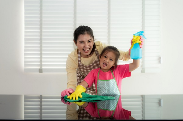 A Hispanic woman and child wearing yellow rubber gloves and holding a water bottle. It looks like they are about to start cleaning. They're enjoying their time together.