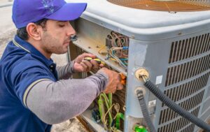 a professional electrician man is fixing the heavy unit of an air conditioner at the roof top of a building and wearing blue uniform and head cap