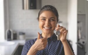 A smiling woman holding a set of house keys in her left hand and giving a thumbs up with her right.