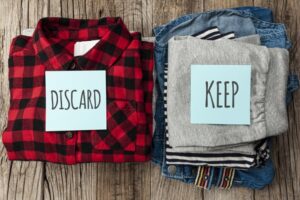 Two piles of folded clothes, one with a discard label and one with a keep label. The discard pile has a black and red flannel shirt, and the keep pile has jeans and gray sweatpants