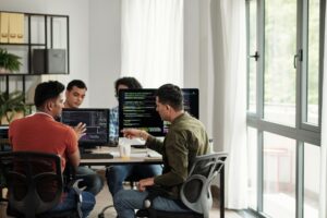 Four male developers sitting around computers discussing code.