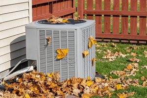 An outdoor air conditioner with autumn leaves strewn about