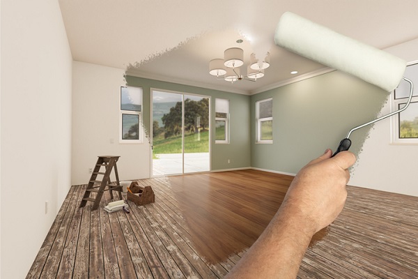 A man's arm with a paint roller. The section his arm has rolled over shows a clean room with a dark hardwood floor and mint-green walls. The sections around the rolled portion show a room with dusty wood floors and plain white walls.