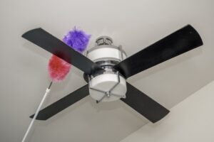 A red and purple duster on an extension pole cleaning the top side of a dark brown ceiling fan