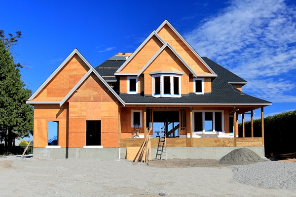 A new, two-story home's wooden frame and black roof shingles. The home has a wraparound porch,