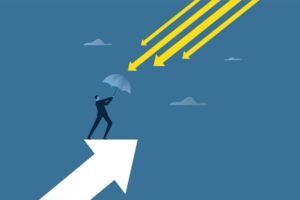 A vector animation. A man in a dark blue suit is standing on a light blue arrow that's pointing toward the top right of the screen. He's holding a blue-gray umbrella in the direction of four gold arrows that are raining down toward him. There are three clouds, the same color as the umbrella, scattered around the blue background