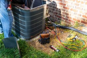 An outdoor air conditioning unit with tools strewn about it. Grass is green.