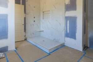 An under construction bathroom, including the floor of the shower, blue tape along the seams of an unfinished bathroom floor, and completed shower tile.