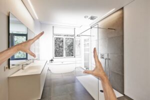 Planned renovation of a Luxury modern bathroom, Bathtub in corian, Faucet and shower in tiled bathroom with windows towards garden. A pair of white hands frames the photo