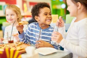 Colorful portrait of multi-ethnic group of children eating pizza enjoying awesome party in pizzeria, focus on Black boy laughing happily