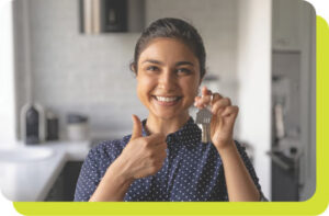 A smiling woman holding a set of keys in her left hand and giving a thumbs up with her right hand.