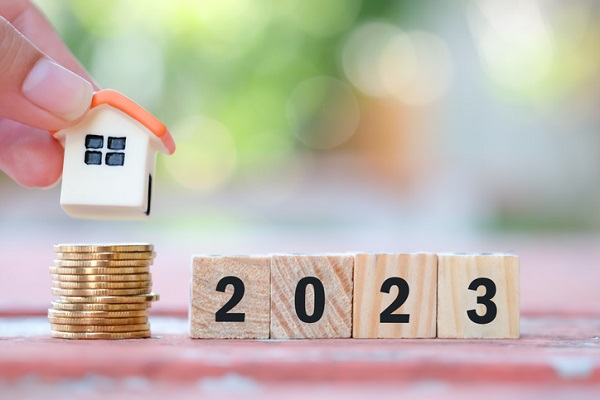 Wooden blocks that spell 2023 next to a stack of coins. a tiny house hovers over the coin stack between two fingers.