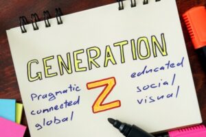 A notepad with the phrase "Generation Z" written in the middle. On the left of the phrase appear the words "pragmatic," "connected," and "global." On the right of the phrase appear the words "educated," "social," and "visual." The notepad rests on a wooden table. A black marker rests on the notepad.