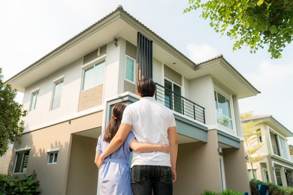 Back portrait of Asian young couple standing and hugging together looking happy in front of their new house to start new life.