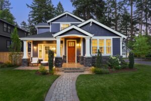 facade of home with manicured lawn, landscaping, and backdrop of trees and dark blue sky. Glowing interior lights create a welcoming mood, signifying a model home that could be affected by SB 360