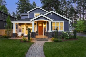 facade of home with manicured lawn, landscaping, and backdrop of trees and dark blue sky. Glowing interior lights create a welcoming mood, signifying a model home that could be affected by SB 360