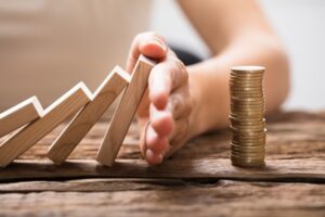 Close-up Of A Businesswoman's Hand Stopping The Wooden Blocks From Falling On Stacked Coins