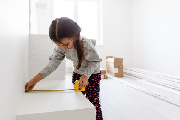 Little smiling girl holding tape-measure apartment repair wall repair remodel house renovation home