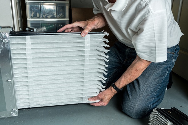 Senior man inserting a new air filter in a HVAC Furnace as part of heating maintenance